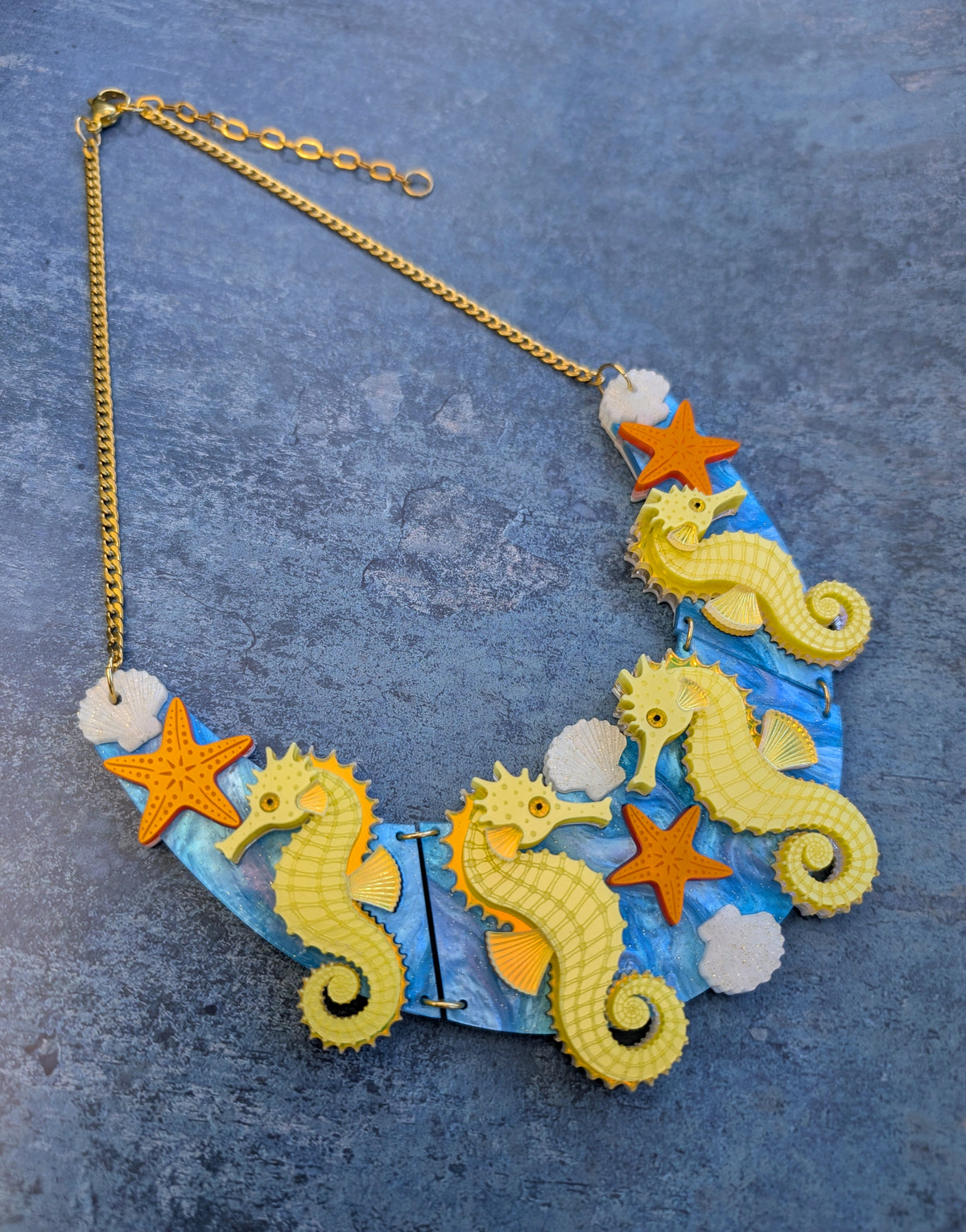 a handmade laser cut acrylic necklace featuring yellow seahorses, orange starfish and cream shells