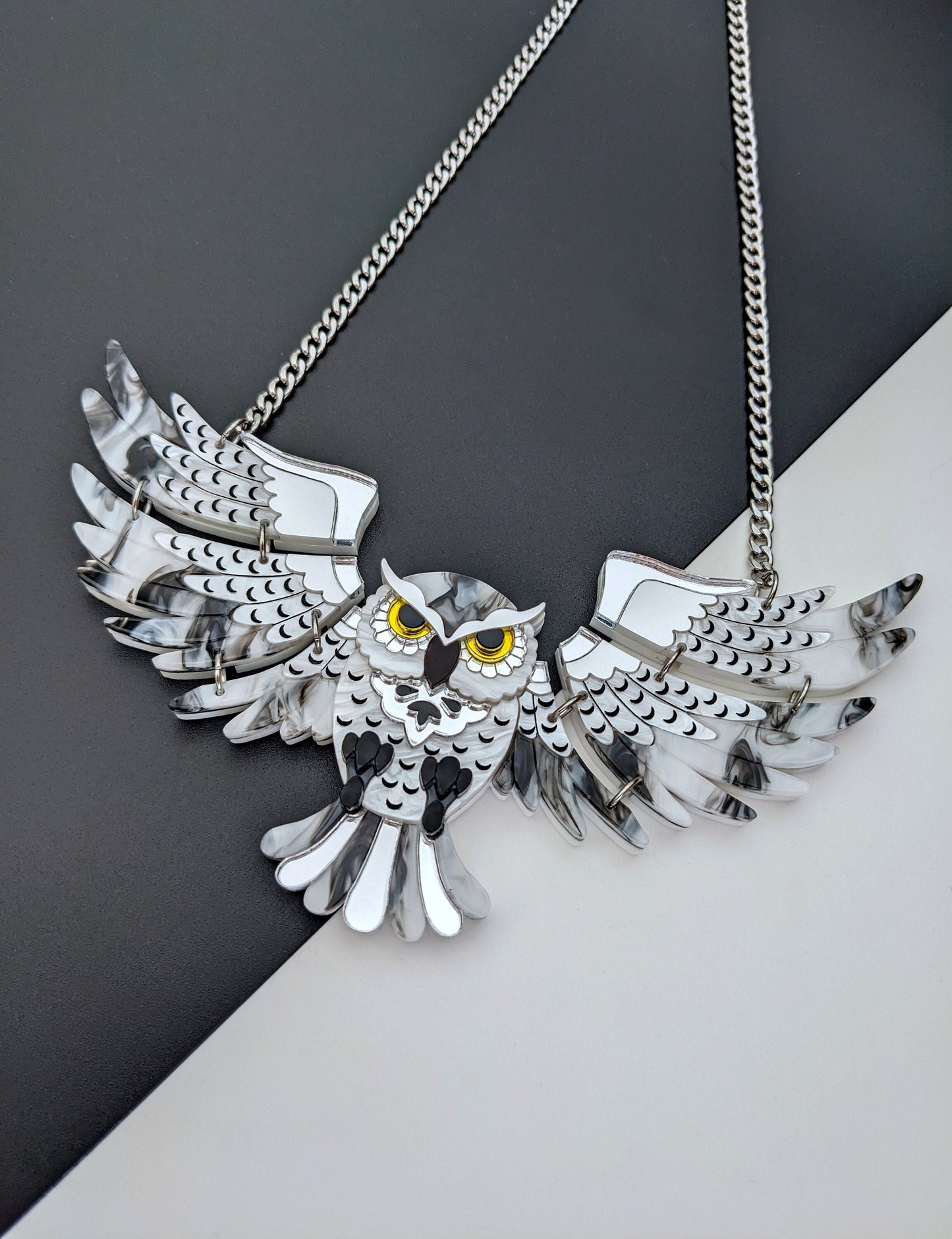A statement owl necklace with silver acrylic wings and a detailed design, hanging from a stainless steel chain.