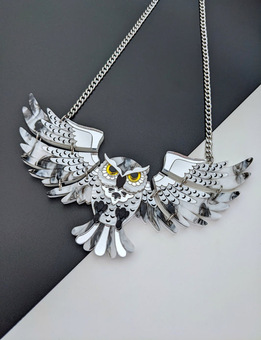 A statement owl necklace with silver acrylic wings and a detailed design, hanging from a stainless steel chain.
