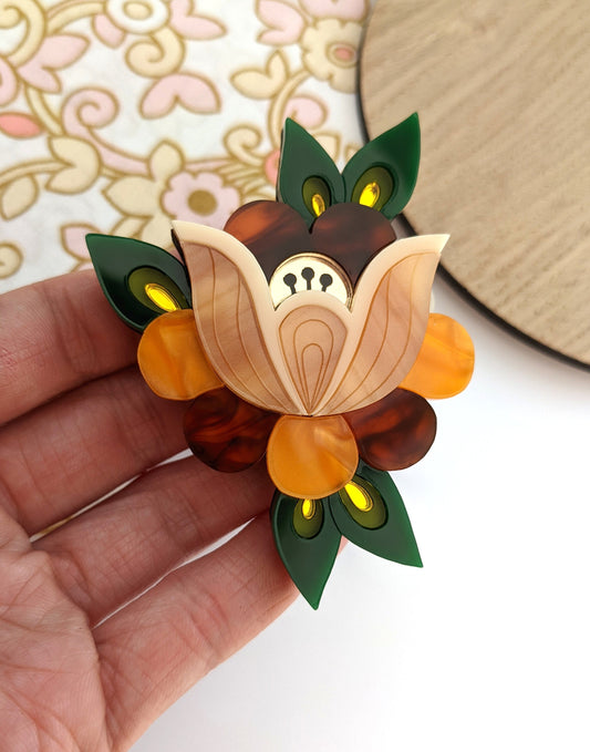 A floral brooch with a mix of pearl marble, faux tortoiseshell, and mirror acrylic in orange, green, and black colors, held in a person's hand.