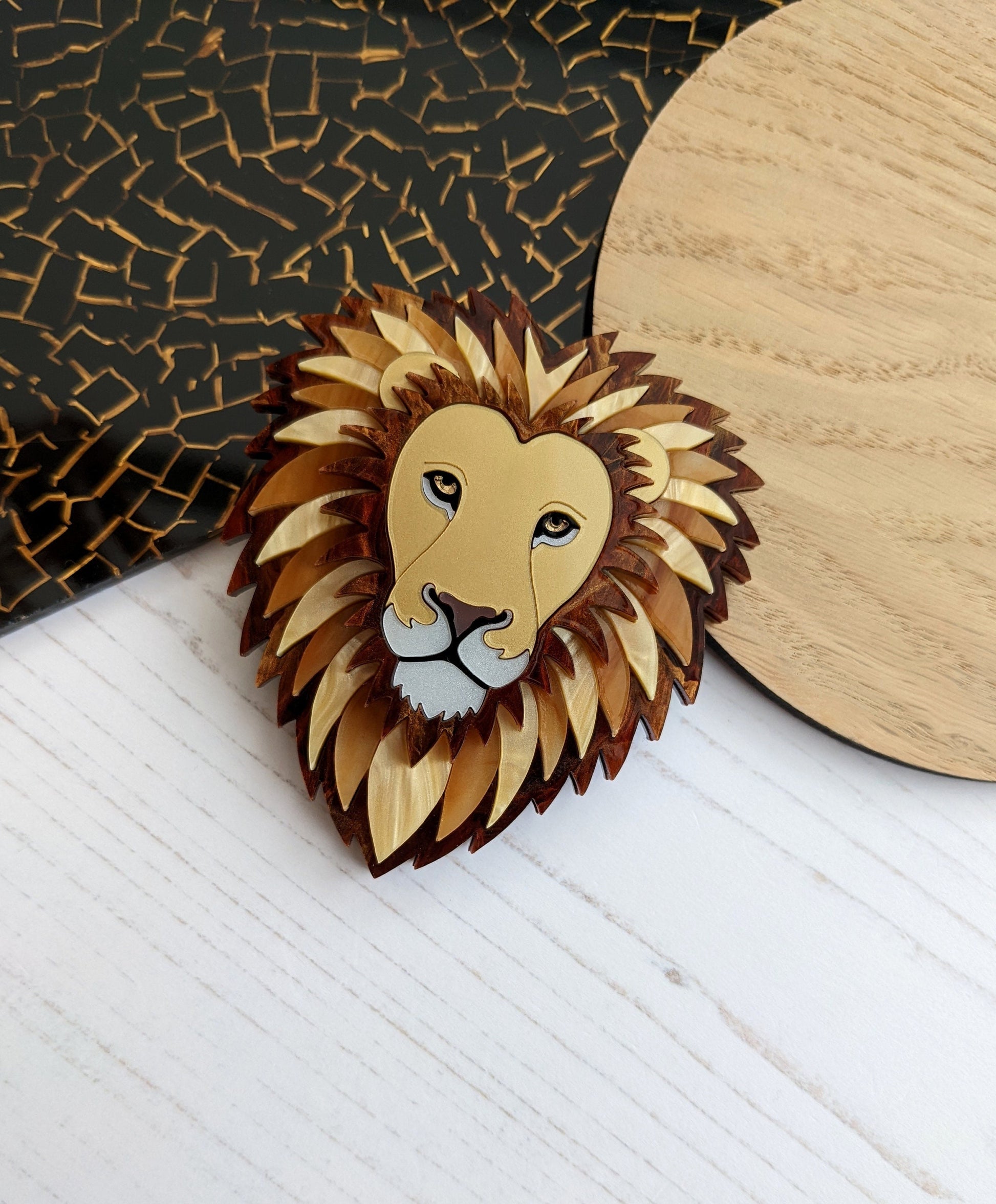 A brooch designed in the shape of a lion's head, with a mane in shades of brown and a gold-colored face.